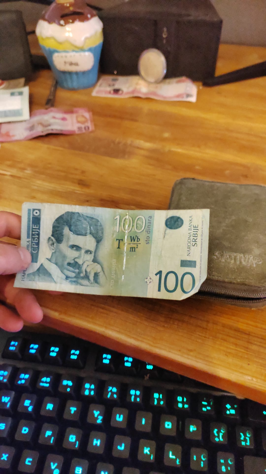 A hand holding a current Serbian 100 dinara banknote with the portrait of Nikola Tesla and his magnetic flux density formula — still legal tender in Serbia today.